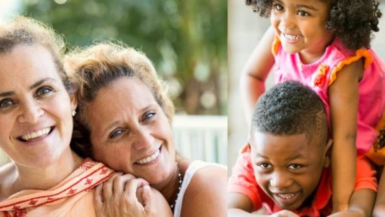 Two women smiling, one leaning on the other's shoulder on the left. On the right, a child in pink smiling on top of another child in red, who is also smiling.
