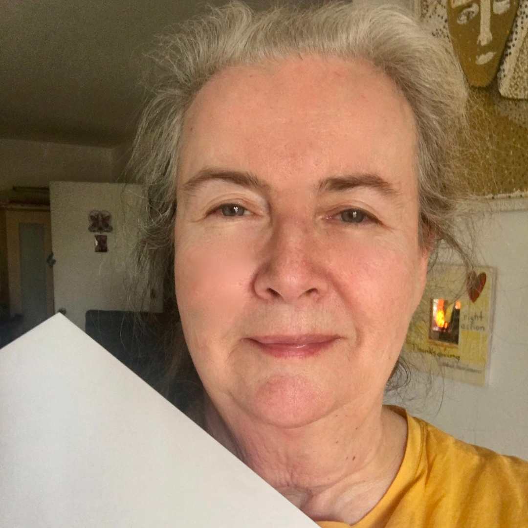 Judy-Square Person with gray hair holding a piece of paper, wearing a yellow shirt, stands indoors.