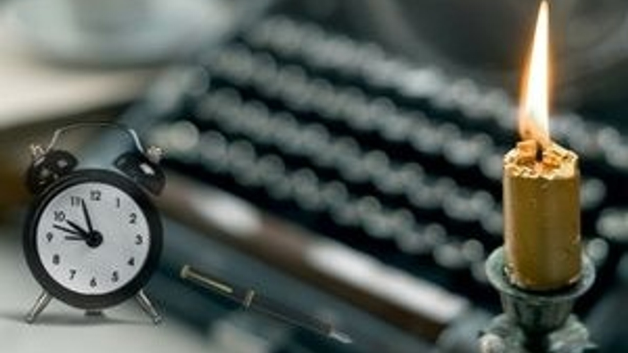 A burning candle, a black alarm clock displaying 10:10, a fountain pen, and an out-of-focus typewriter in the background.