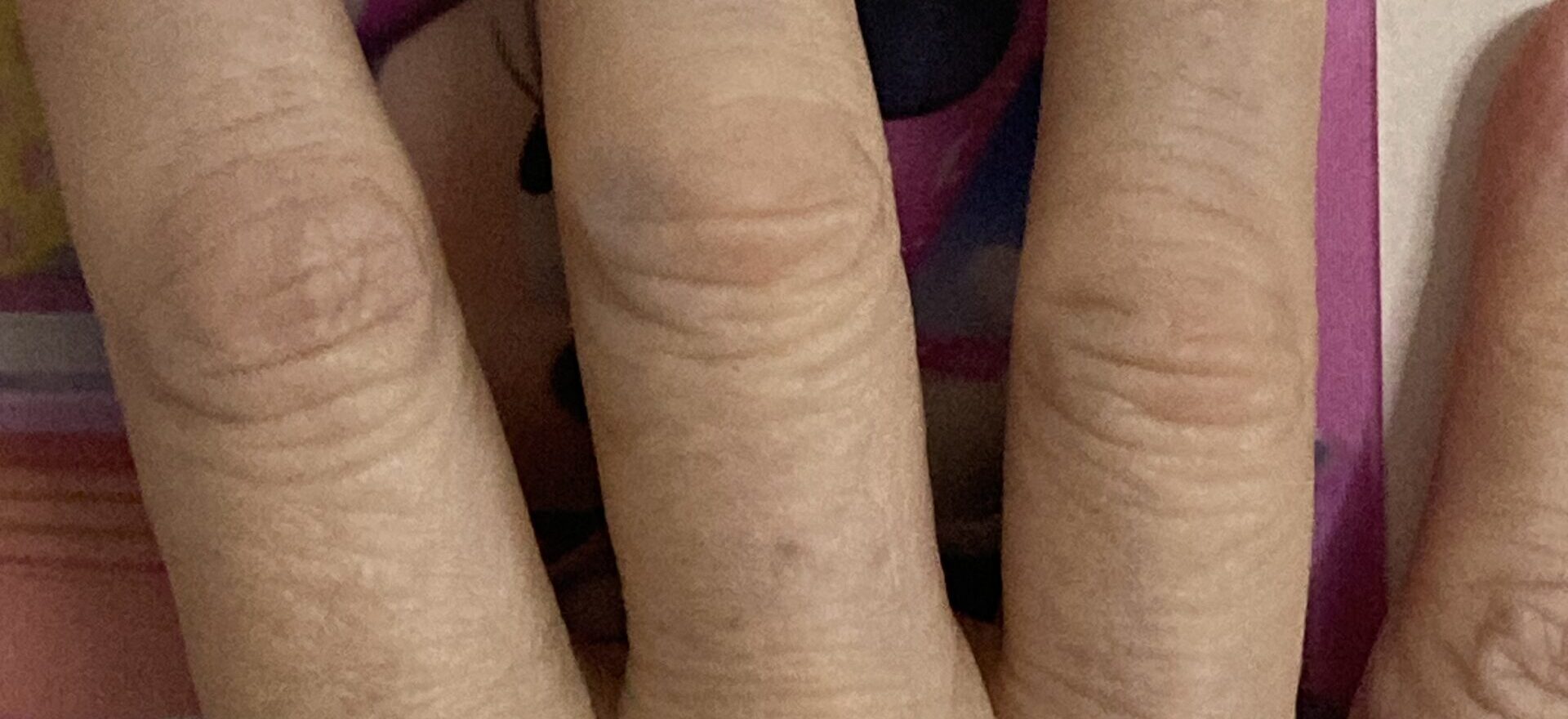 A close-up of three fingers resting on a colorful, cartoon-patterned surface.